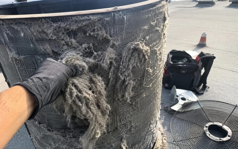 Condenser coil packed with grease, lint, and cottonwood fluff before summer cleaning