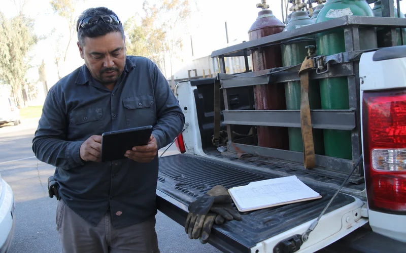 Delivery driver checking a route schedule beside gas cylinders in the truck