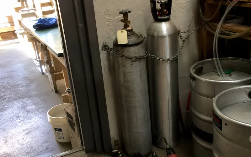 Empty and full CO2 cylinders side by side during a mid-shift swap in a Portland bar cellar
