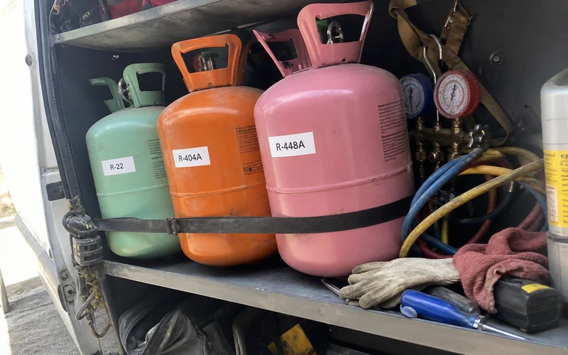 Refrigerant cylinders labeled R-22, R-404A, and R-448A on a service van shelf