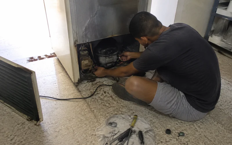 Technician performing an out-of-warranty repair on an older commercial cooler