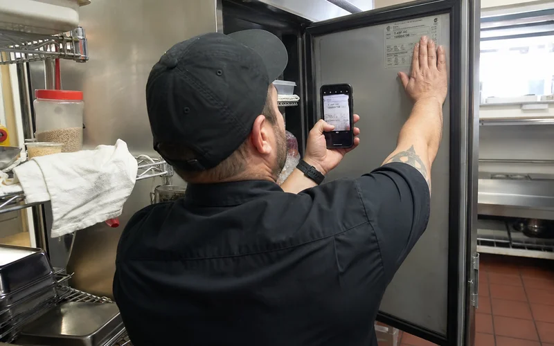 Technician reading the model and serial data plate inside a commercial refrigerator