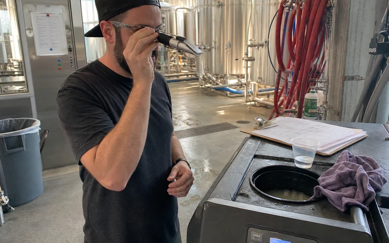 Technician testing glycol concentration with a refractometer at a brewery chiller reservoir