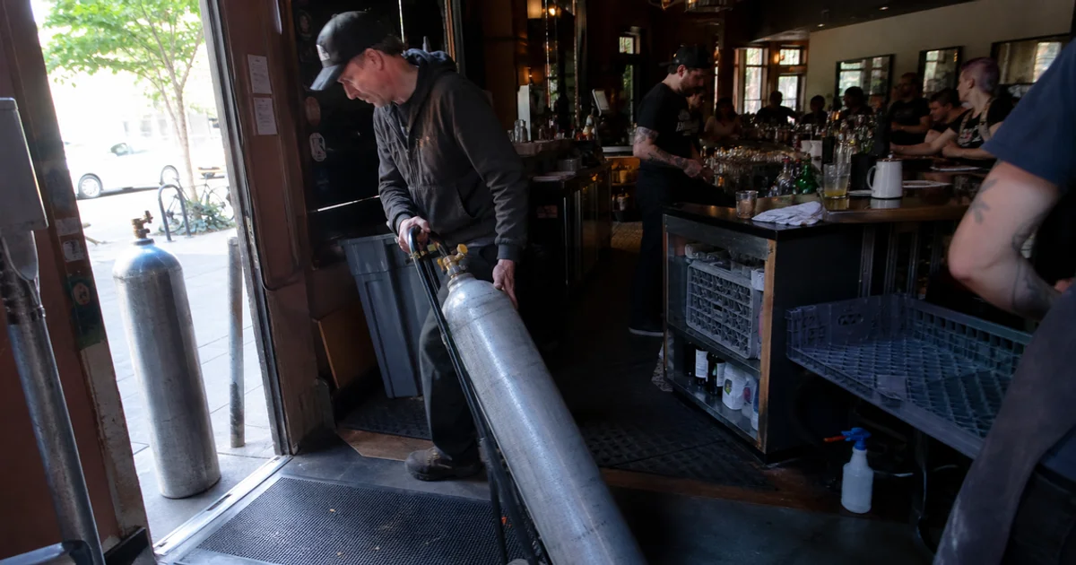 Delivery driver bringing a replacement CO2 cylinder into a busy Portland bar