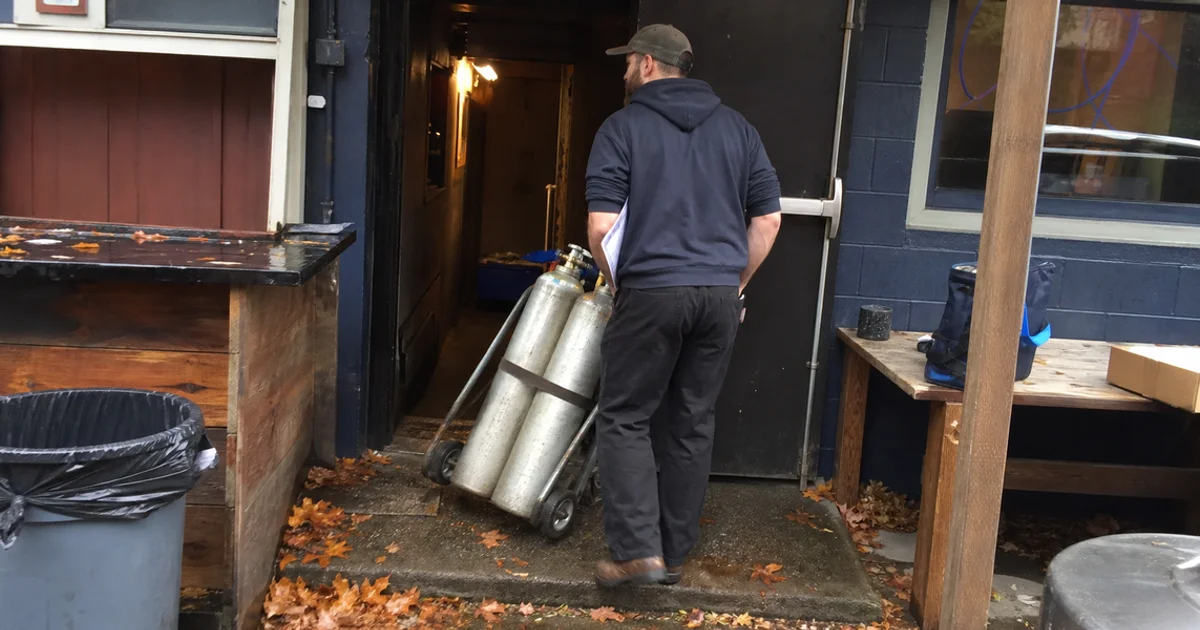 Gas delivery driver bringing full CO2 cylinders into a Portland bar on a scheduled route stop