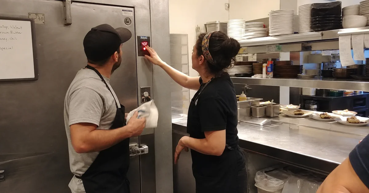 Kitchen staff responding to a flashing walk-in freezer temperature alarm panel during service