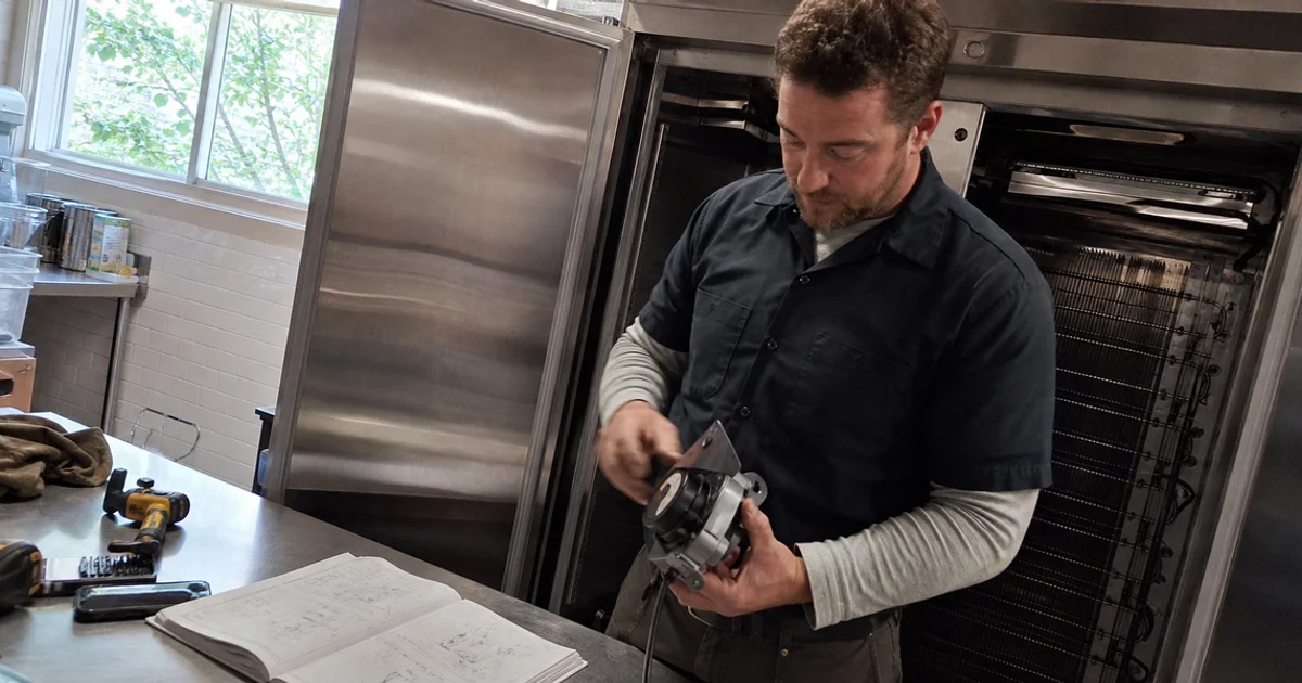 Manufacturer-certified technician servicing a branded commercial refrigerator under warranty