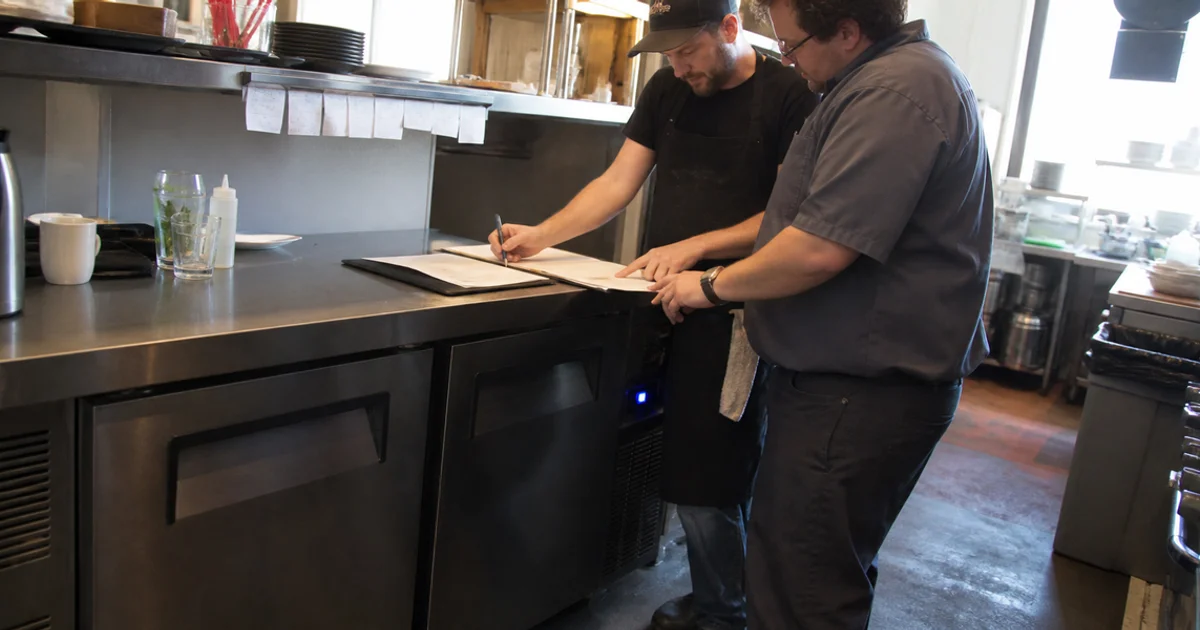 Restaurant owner and technician reviewing warranty paperwork beside a commercial unit