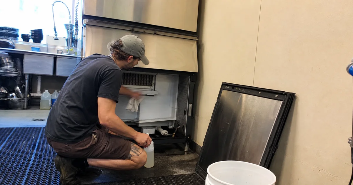 Technician cleaning and sanitizing the interior of a commercial ice machine