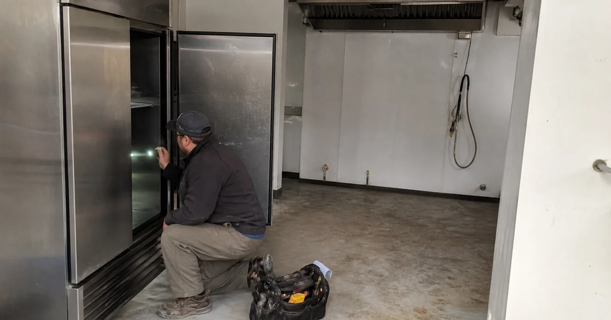Technician inspecting used commercial refrigeration equipment in an empty leased kitchen