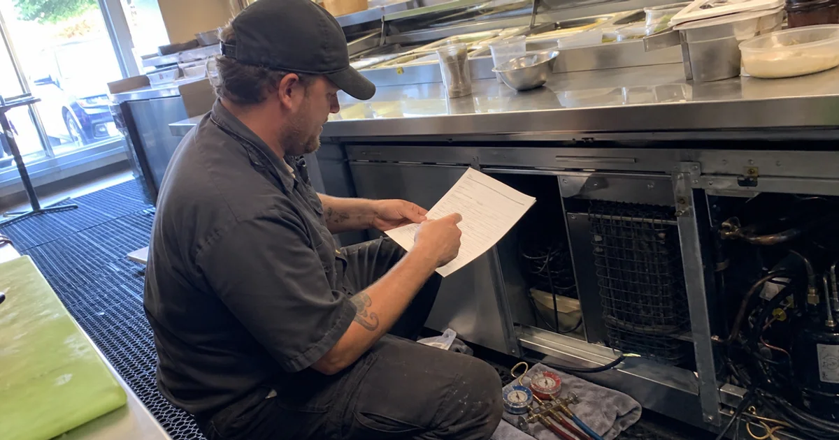 Technician performing scheduled maintenance on a commercial cooler with a checklist