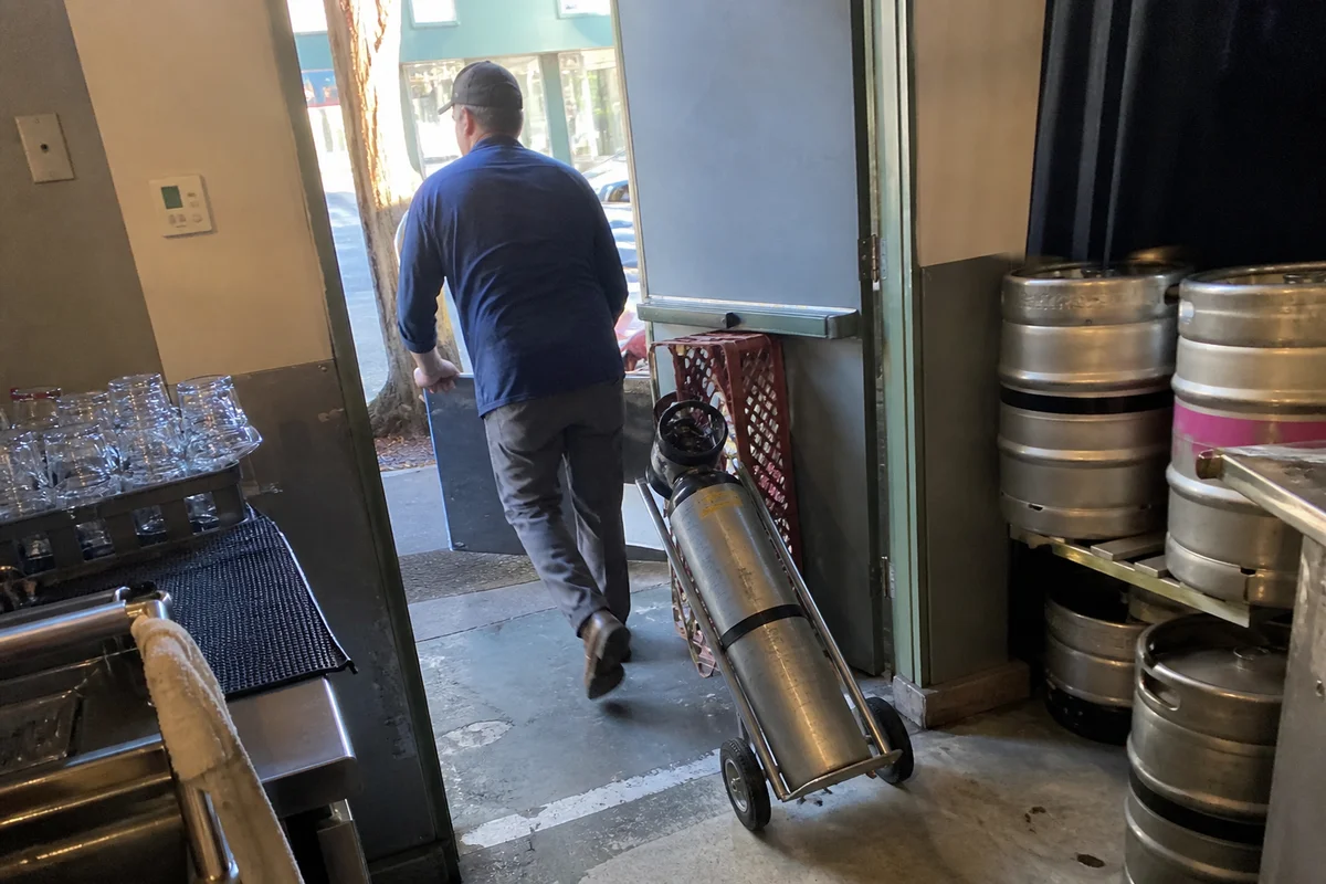 Driver delivering a full CO2 cylinder to a Portland bar on a scheduled gas route