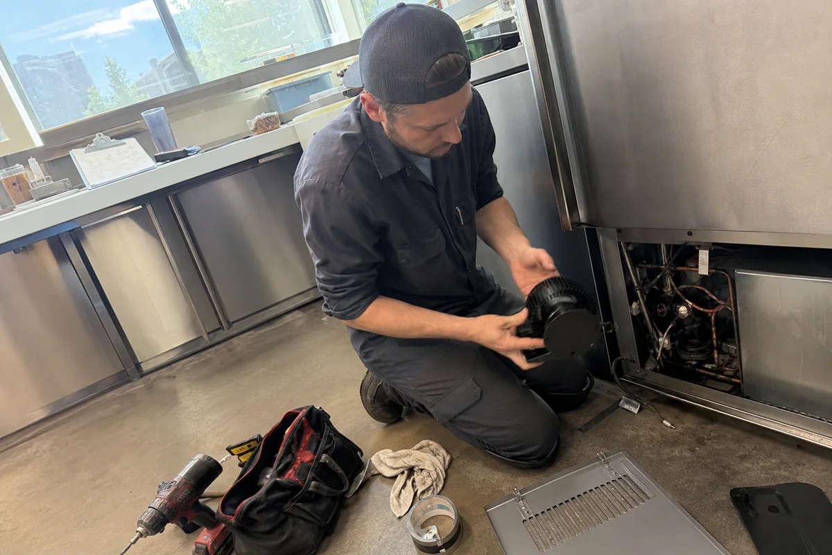 Manufacturer-certified technician performing warranty service on a branded commercial refrigerator