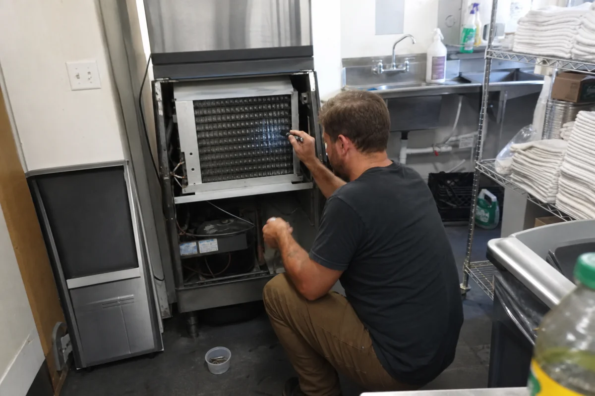 Technician inspecting the evaporator grid inside a commercial ice machine in a Portland bar